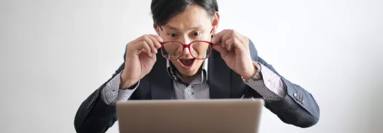 Man with red glasses looking surprised at a laptop screen.